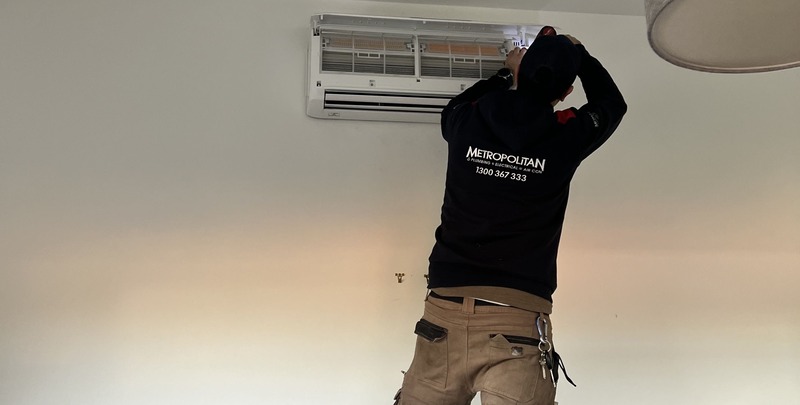 A Metropolitan Heating and Cooling tech works on an air conditioner